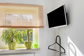 Una habitació amb televisió penjada a la paret, una finestra amb persianes i un radiador.