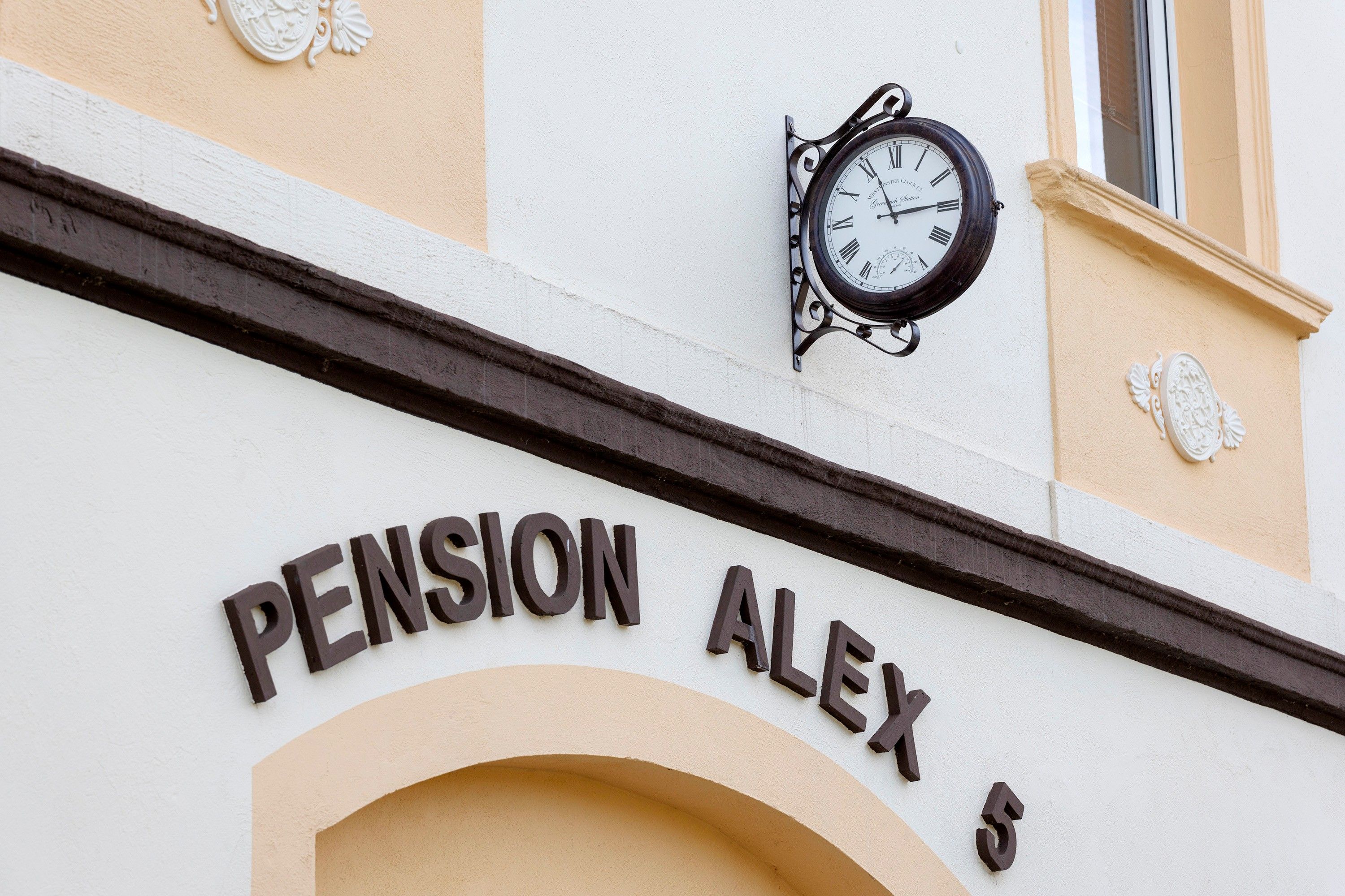 Un bâtiment avec une enseigne indiquant « PENSION ALEX 5 » et une horloge fixée au mur.