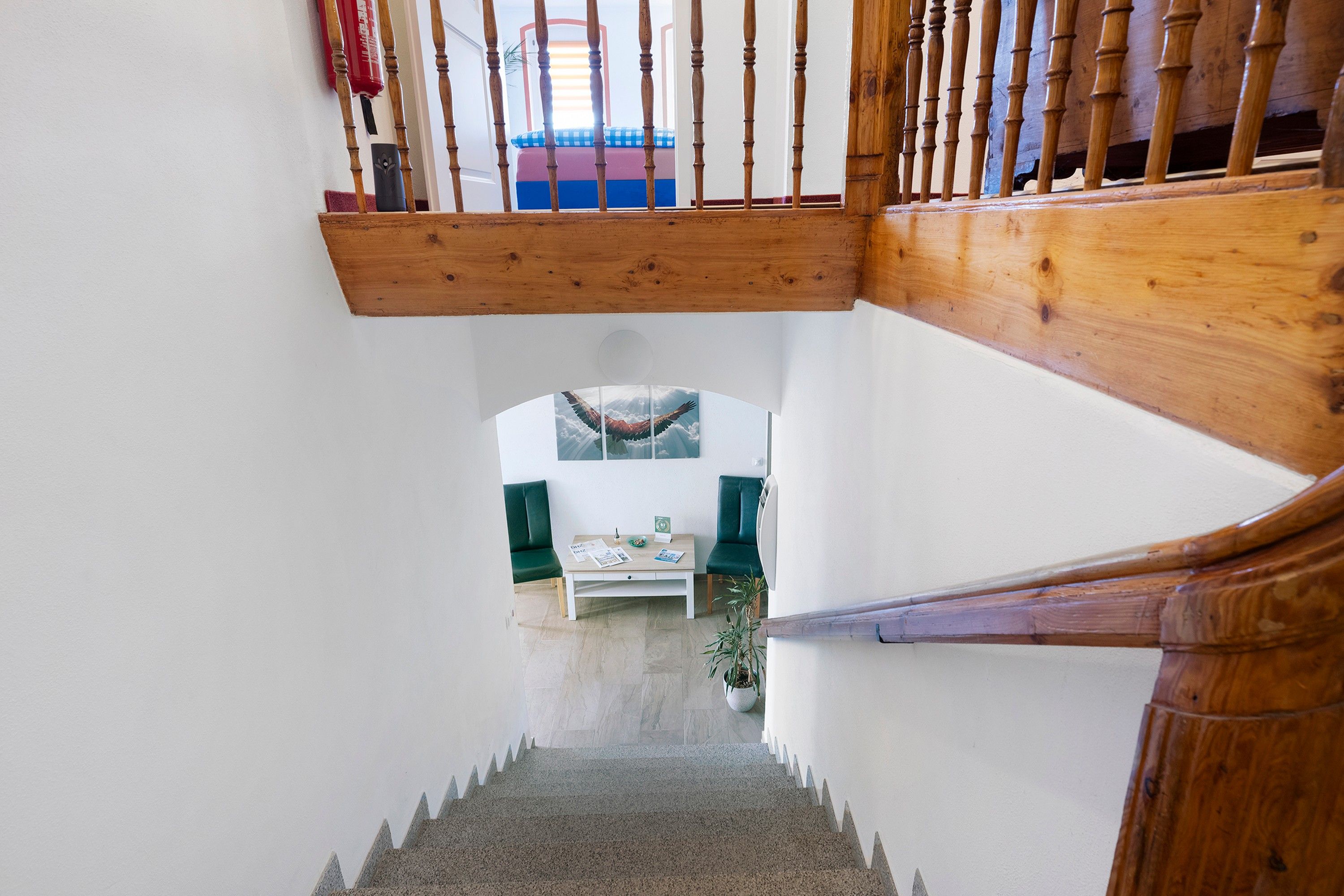 A staircase with wooden balusters leading to a landing where a green chair and a table with a plant are placed.