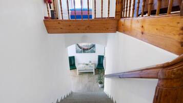 A staircase with wooden balusters leading to a landing where a green chair and a table with a plant are placed.