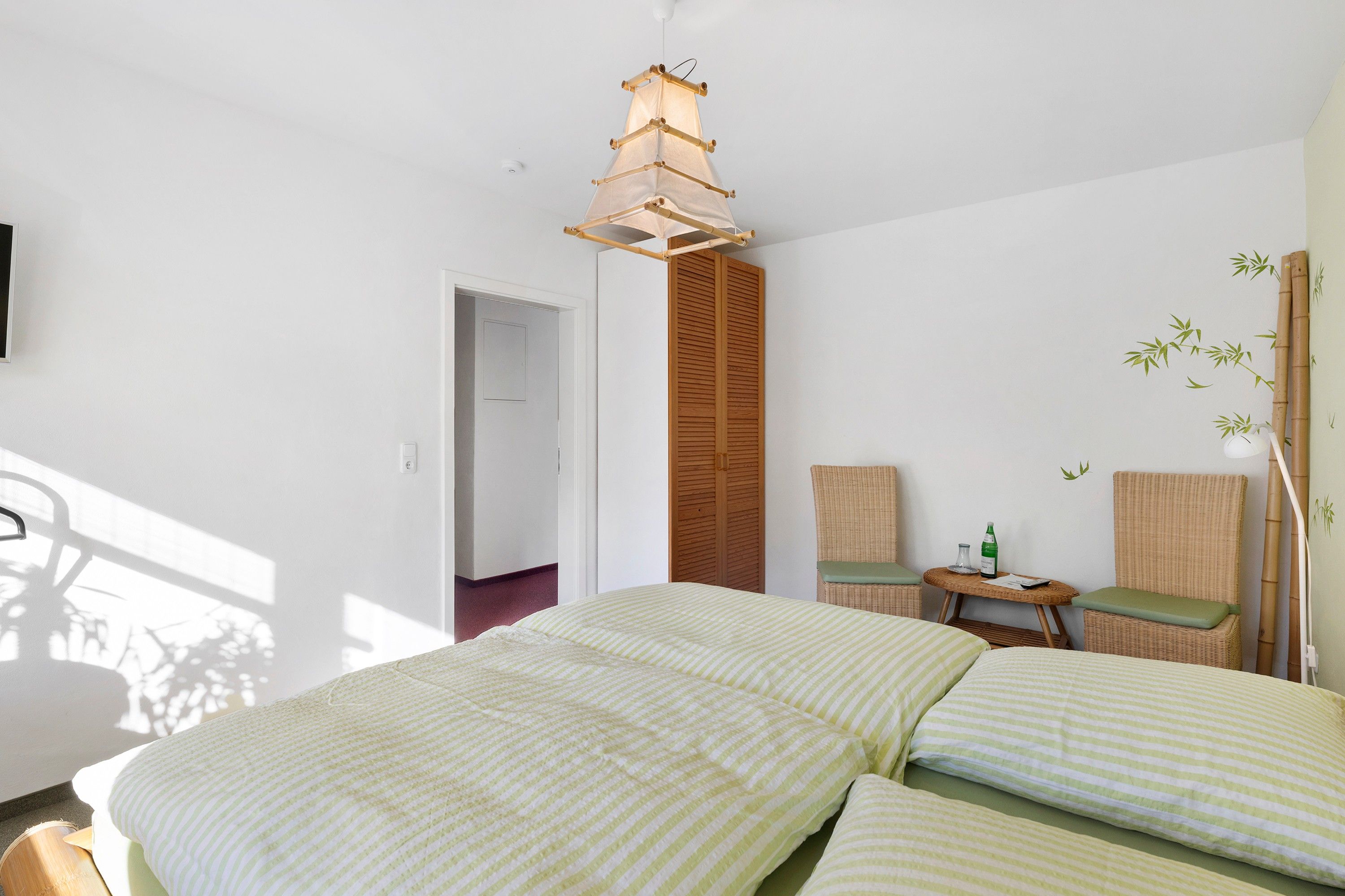 A hotel room with a bed, two chairs, a small table, and a wall-mounted lamp.