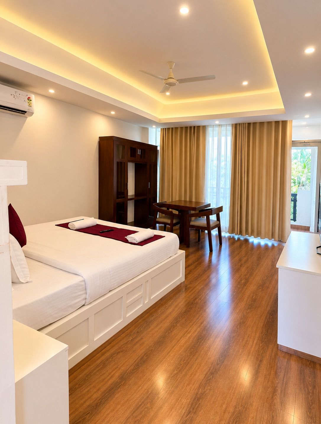 Habitación de hotel con cama, escritorio, silla, ventilador de techo y una ventana grande con cortinas.