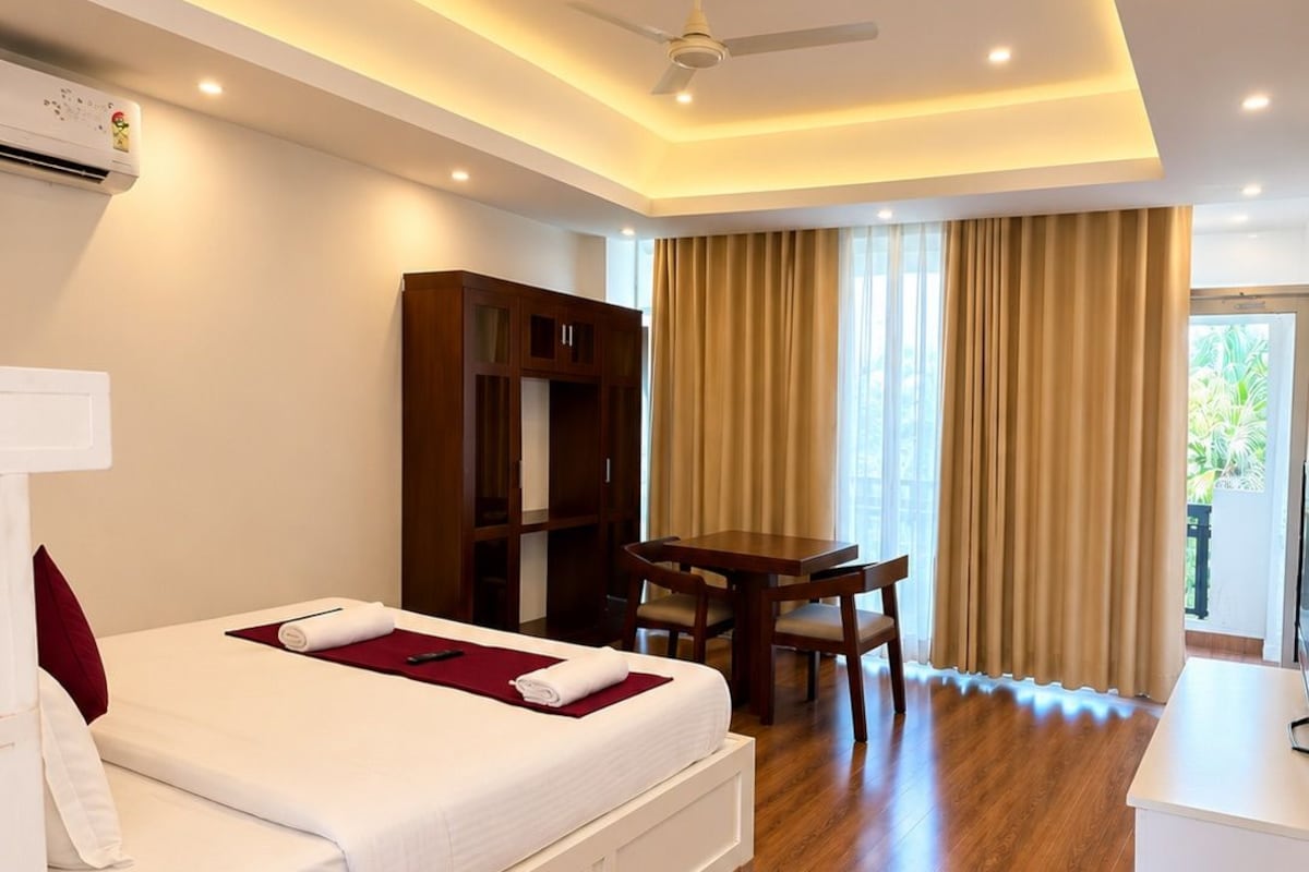 A hotel room with a bed, a desk, a chair, a ceiling fan, and a large window with curtains.