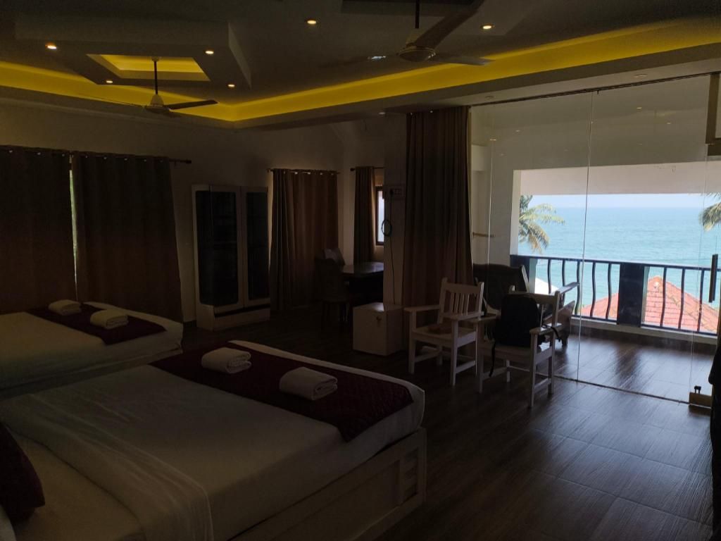 Habitación de hotel con dos camas, un escritorio, una silla y un balcón con vista al mar.