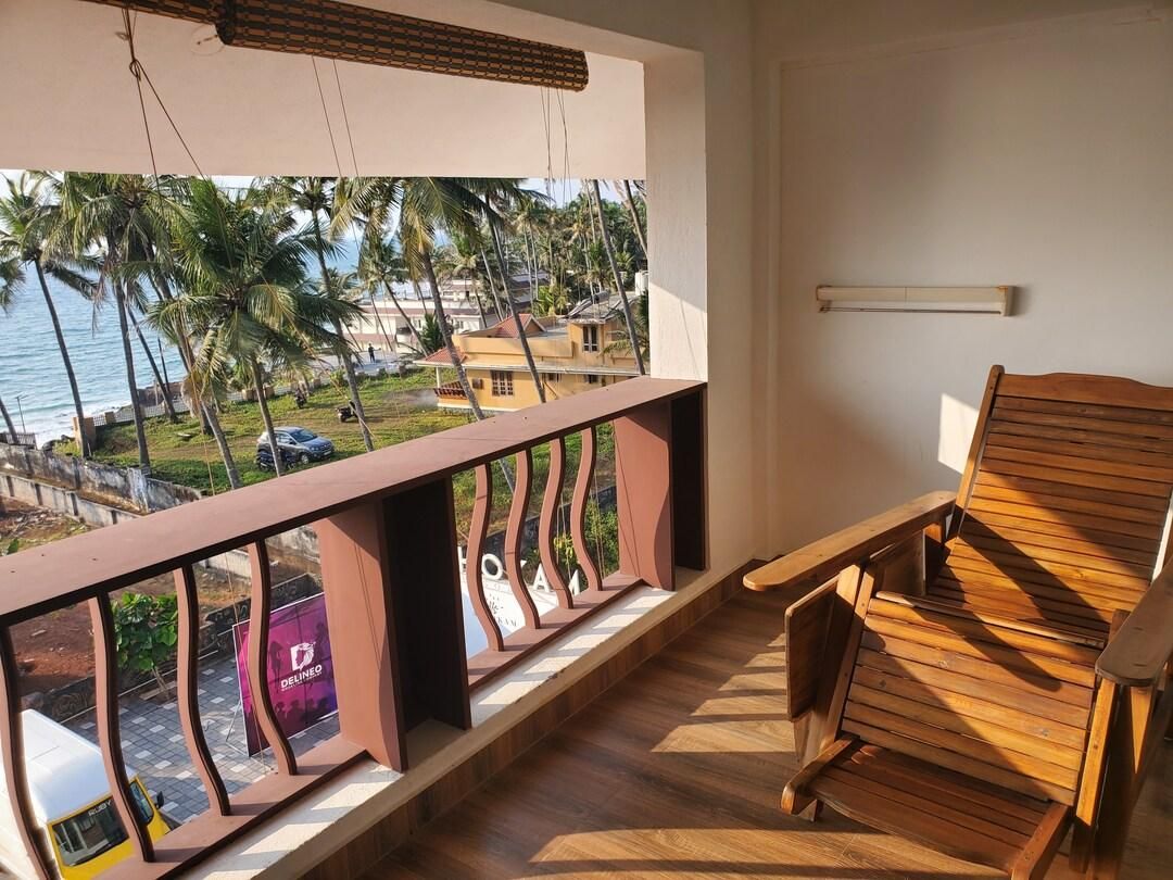 A balcony with a view of the sea and palm trees, wooden furniture, and a hanging light fixture.