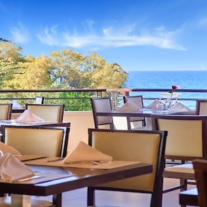 Un restaurant amb terrassa a l'aire lliure amb vistes al mar, amb taules i cadiretes.