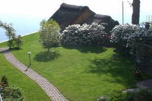 Ein traditionelles Haus mit einem Reetdach, verbunden durch einen gepflasterten Weg, umgeben von gepflegtem Rasen und blühenden Büschen.
