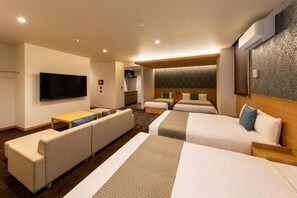 Una habitación de hotel con televisión de pantalla plana, un sofá, dos camas y una kitchenette pequeña.