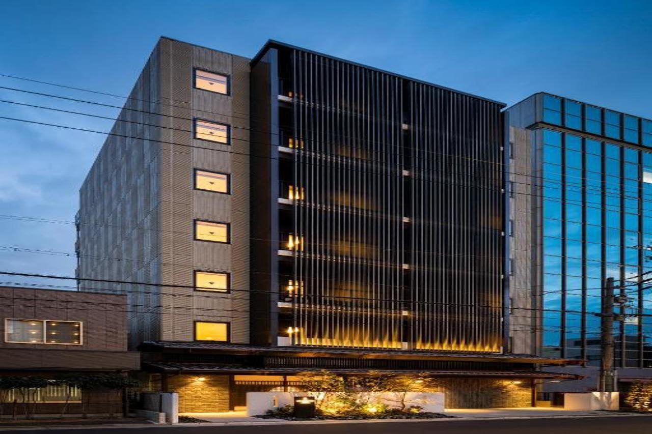 A modern building with a vertical facade, multiple windows, and a ground-level entrance with outdoor lighting.