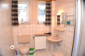 Un bagno piccolo con il water, un lavandino e un termosifone. Ci sono due finestre con tende e uno specchio sopra il lavandino.