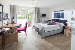 Une chambre à coucher avec un lit, un bureau, une chaise, un téléviseur et une fenêtre avec des rideaux.