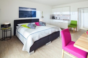 A modern hotel room with a bed, bedside table, and a view of the kitchen area. - Apartment in Juist with Wi-Fi and fishing (Juist)