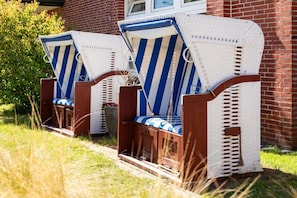 Two wicker chairs with blue and white striped cushions, positioned on a grassy area in front of a brick building. - Apartment in Juist with Wi-Fi and fishing (Juist)