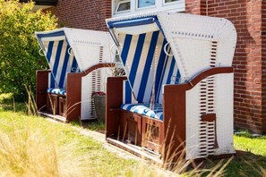 Two wicker chairs with blue and white striped cushions, positioned in front of a brick building. - Apartment in Juist with swimming pool (Juist)