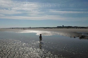 A beach scene with a child walking in shallow water, distant buildings, and a clear sky. - Apartment in Juist with swimming pool (Juist)