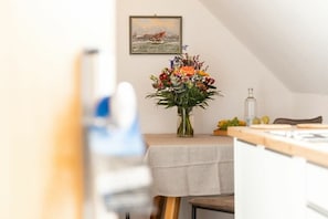 A dining area with a table set for two, a vase of flowers, and a painting on the wall. - Apartment in Juist with swimming pool (Juist)