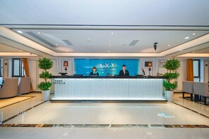 Een receptiebalie van een hotel met een modern ontwerp, twee receptionisten en een blauwe achtergrond met de naam van het hotel.