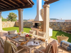An outdoor patio with a stone wall, a table set for dining, and a view of the landscape. - Click Sardegna Villa SeaSky – Sea View with Garde (Alghero)