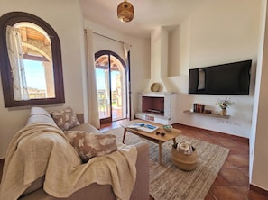 A living room with a sofa, a coffee table, a fireplace, and a television mounted on the wall. - Click Sardegna Villa SeaSky – Sea View with Garde (Alghero)
