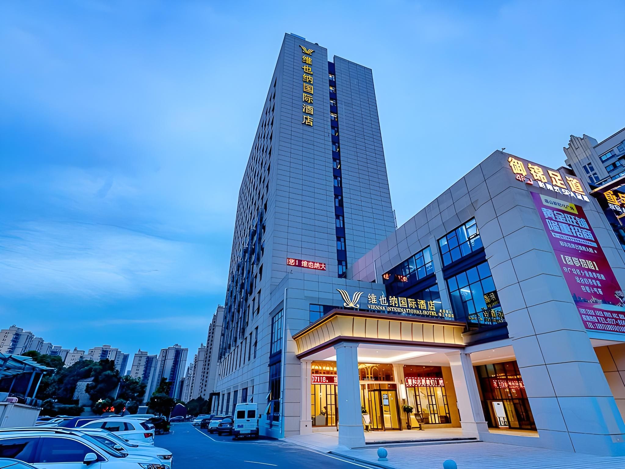 Un hotel moderno con un letrero vertical llamativo, una entrada bien iluminada y un estacionamiento al frente.