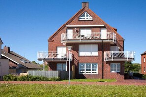 A two-story brick house with a balcony on the upper floor, a visible chimney, and a number '33' on the door. - Holiday apartment Juister Gezeiten (Juist)