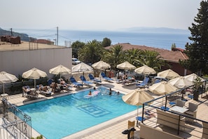 A pool area with sun loungers and umbrellas, a clear view of the sea, and a tiled deck. - Saoulas Studios (Kefalonia)
