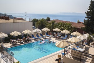 Zona de piscina con tumbonas y sombrillas, vistas despejadas al mar y una terraza con baldosas.