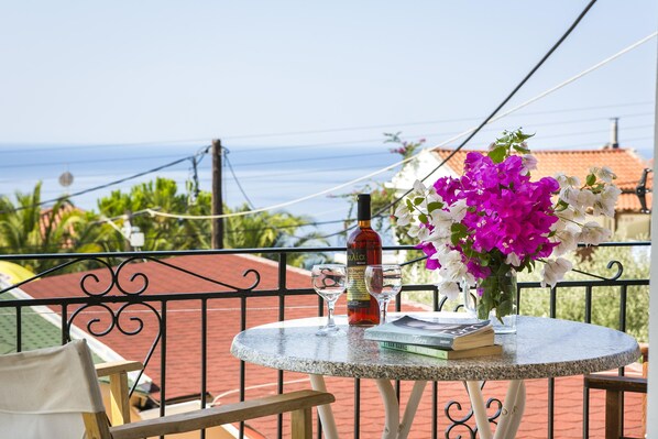 A round table with a bottle, glasses, and books on a balcony overlooking a coastal view. - Saoulas Studios (Kefalonia)