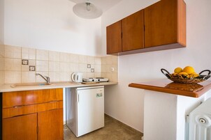 Cocina funcional con lavabo, estufa y refrigerador, armarios de madera y una cesta de frutas sobre la encimera.
