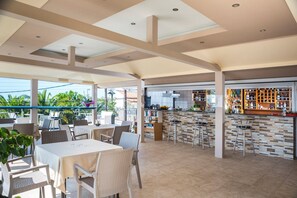 Ein Essbereich im Freien mit Tischen und Stühlen, eine Bar mit Hockern und eine Küche im Hintergrund.