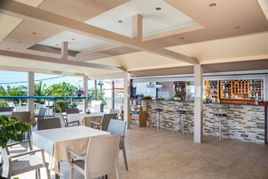 Un área de comedor al aire libre con mesas y sillas, un bar con taburetes y una cocina al fondo.