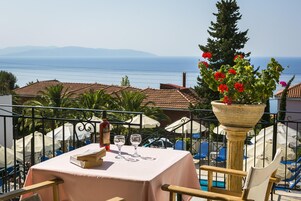 Una mesa con un libro y copas de vino, con vistas a la costa, casas y un cielo despejado.