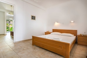 A bedroom with a wooden bed, bedside tables, and a view of a garden through an open door. - Saoulas Studios (Kefalonia)