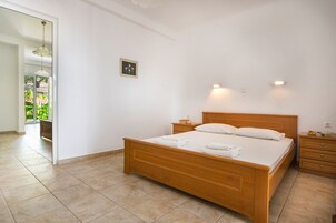 Un dormitorio con cama de madera, mesitas de noche y vista a un jardín a través de una puerta abierta.