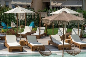 Zona junto a la piscina con sillones de descanso, sombrillas y una terraza de madera.