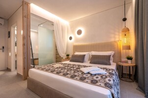 Una habitación de hotel moderna con una cama grande, una mesita de noche con lámpara y una zona de ducha de vidrio.