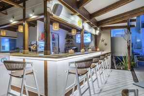 Una zona de bar con una barra larga, varios taburetes y una pantalla de televisión.