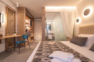 A hotel room with a bed, a chair, a desk, and a bathroom visible through a glass door.