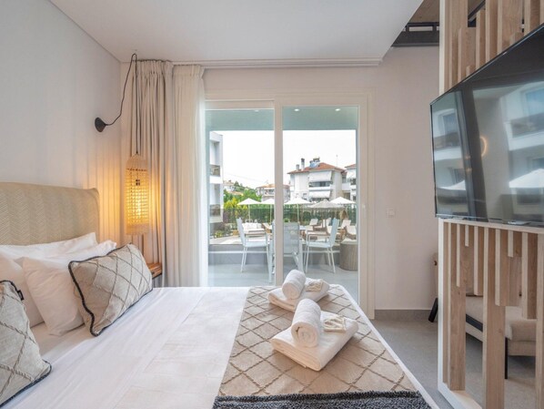 Habitación de hotel con cama, televisión, balcón con mobiliario exterior y vistas a edificios.