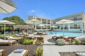 A poolside area with sun loungers, umbrellas, and a modern building in the background. - Mirablue Deluxe Residences (Kassandra)