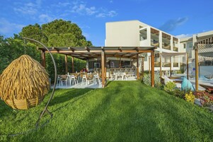 A modern outdoor dining area with a pergola, a hanging chair, and a poolside seating area.