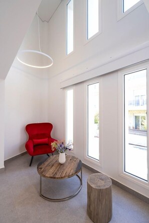 Una habitación moderna con una silla roja, una mesa redonda de madera con un florero y un taburete de madera.