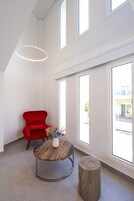 A modern room with a red chair, a round wooden table with a vase, and a wooden stool.