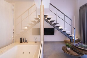 Un interior moderno con una escalera de cristal, una bañera y una mesa de madera con objetos decorativos.