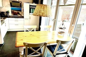 A modern kitchen with white cabinetry, a wooden dining table, and chairs. - Holiday apartment with 1 bedroom (Norddeich)