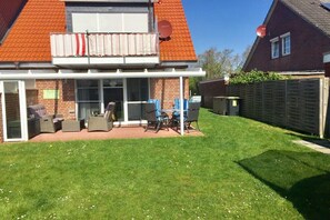A house with a covered patio, outdoor furniture, and a well-maintained lawn. - Holiday apartment with 1 bedroom (Norddeich)
