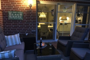 Un espace extérieur aménagé avec des meubles en osier, une table en verre et une bouteille de vin.