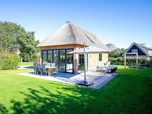 Ein modernes Haus mit einem Strohdach, einer Terrasse mit Gartenmöbeln und einem gepflegten Rasen.