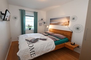 Ein aufgeräumtes Schlafzimmer mit einem Bett, einem Nachttisch und einem an der Wand befestigten Regal mit Pflanzen.