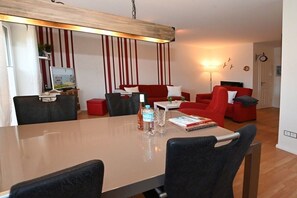 Ein modernes Wohnzimmer mit Esstisch, roten Sofas und einem Fernseher.